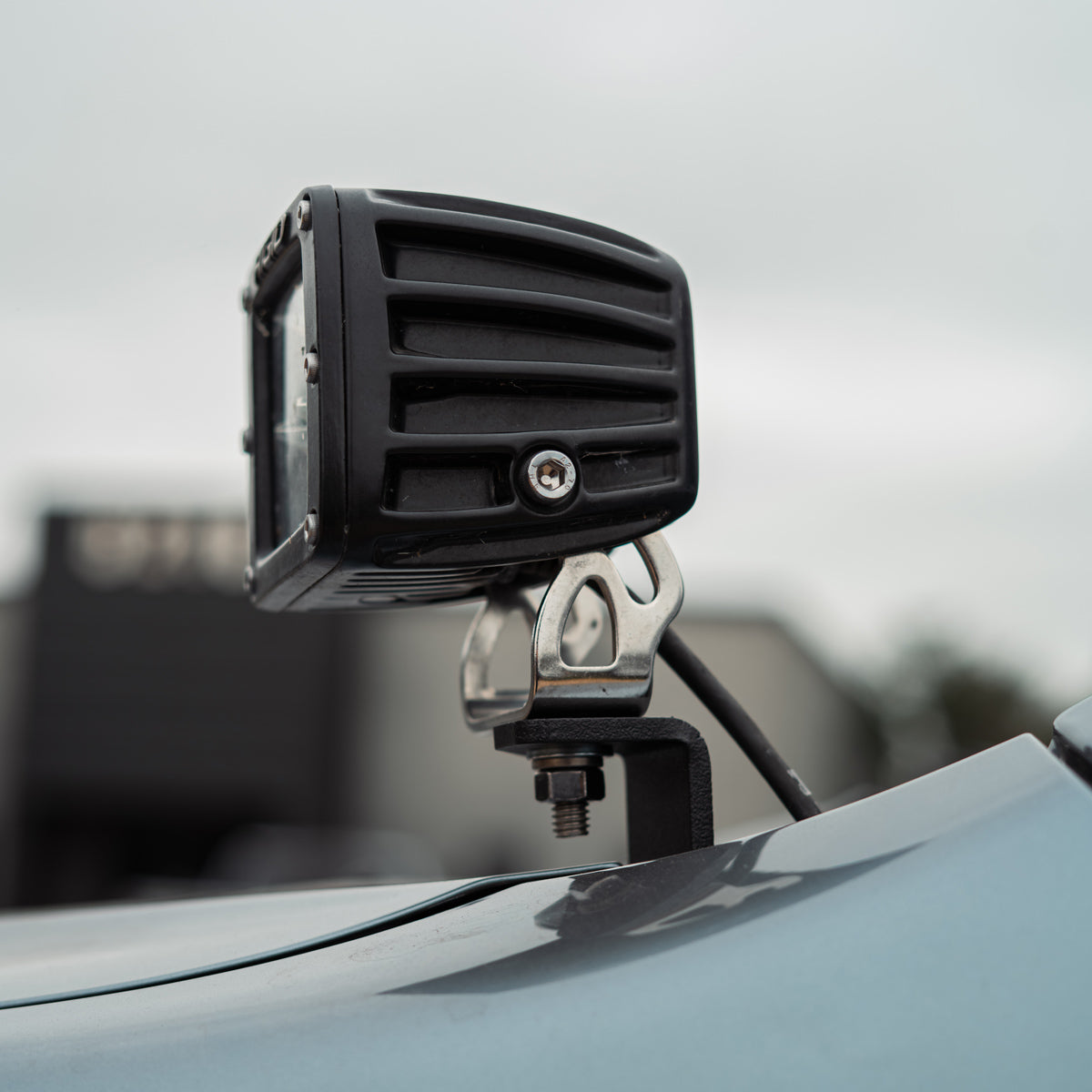 Close view of a black LED pod on a steel ditch light bracket bolted to the hood