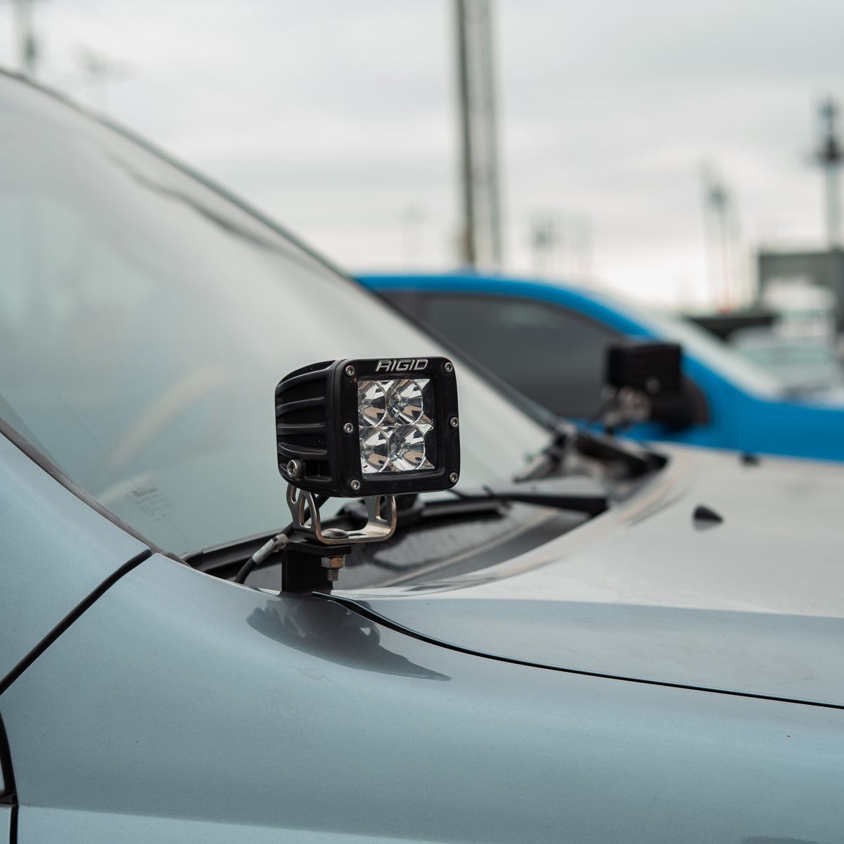 LED pod mounted on a hood-corner bracket beside the windshield of a blue-gray SUV