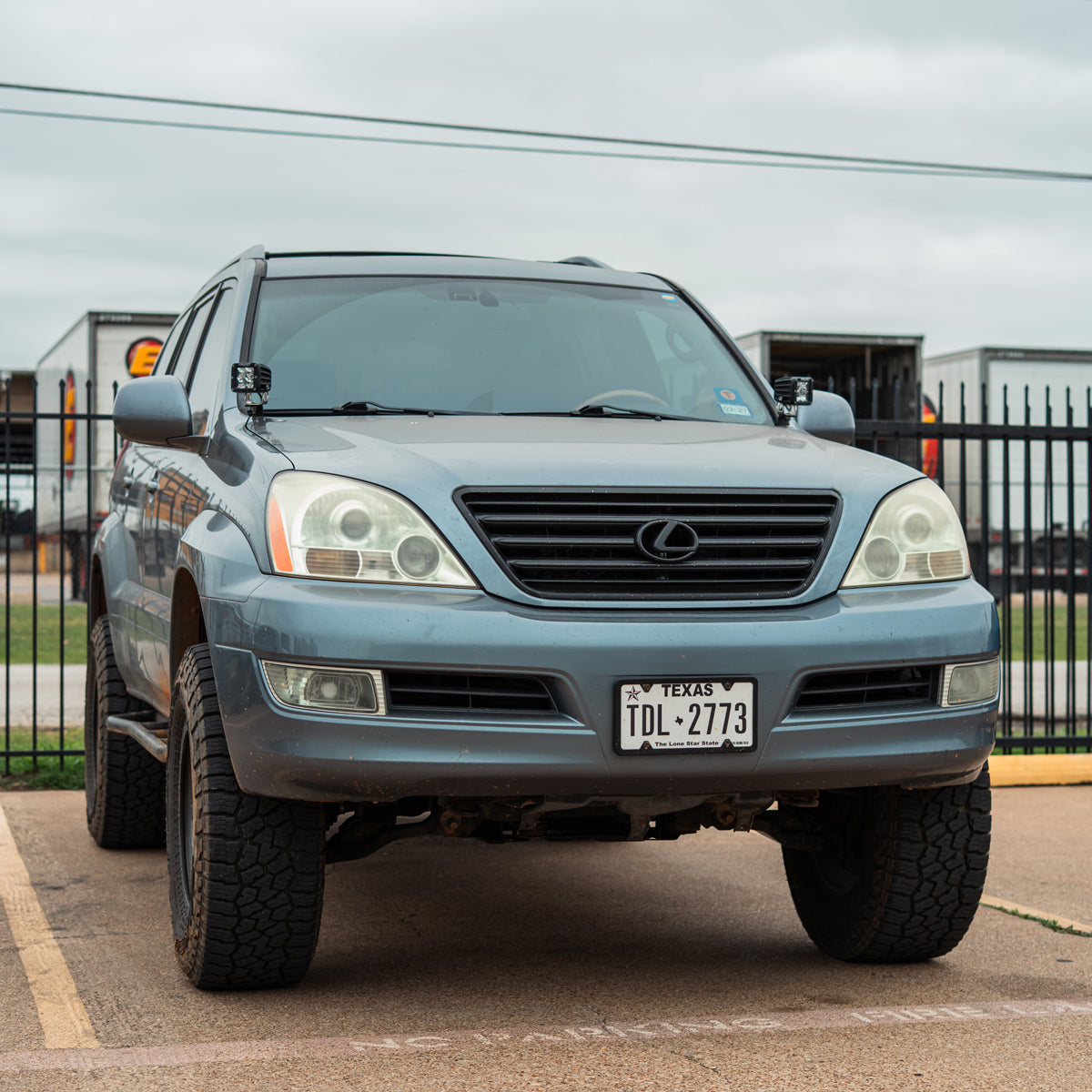Front view of a blue-gray Lexus SUV parked outside with small LED pods mounted on the hood corners