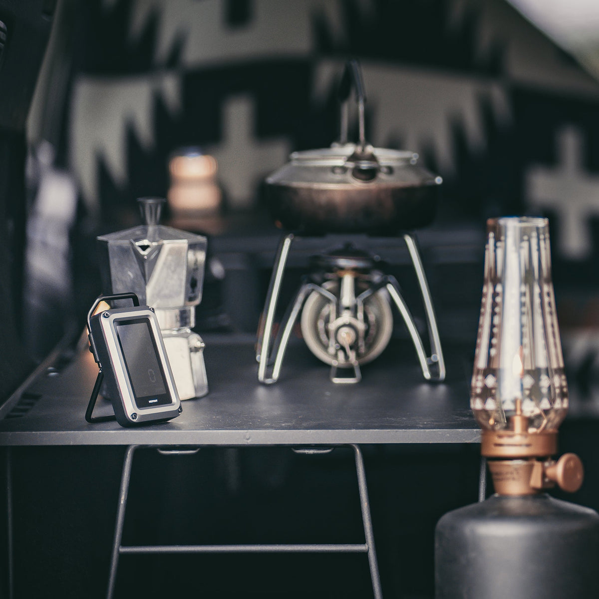 NESTOUT CO Alarm resting on a shelf beside a stovetop espresso maker, a camp stove, and an oil lantern
