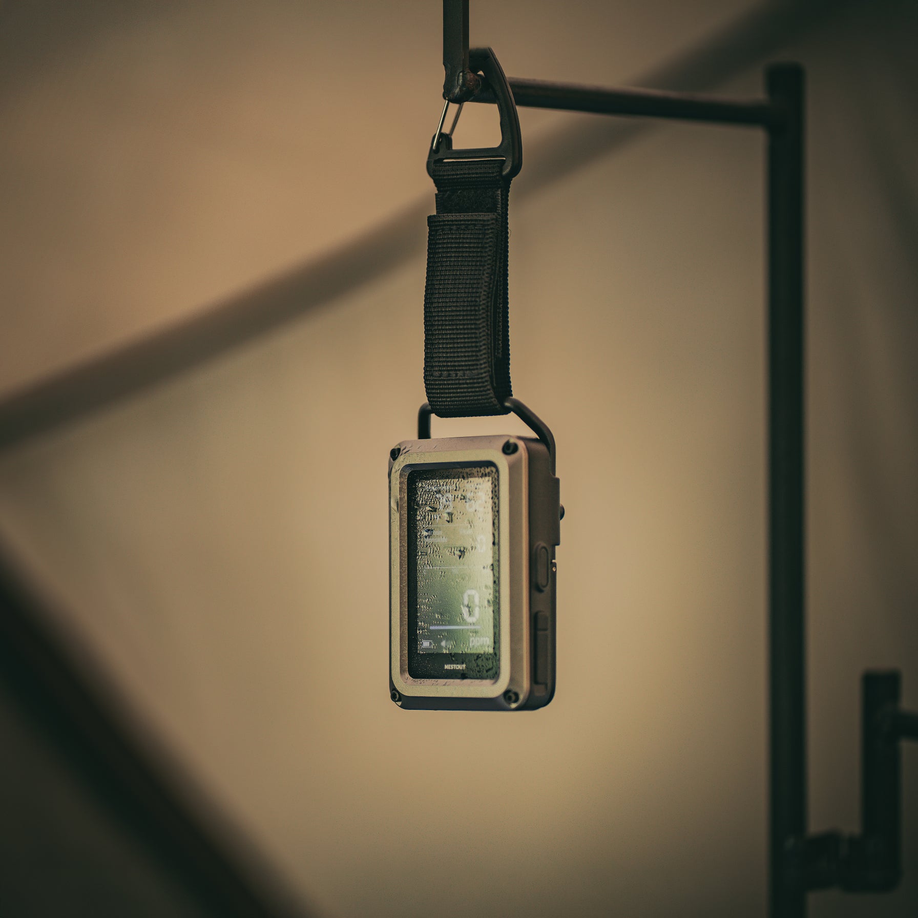 NESTOUT CO Alarm hanging from a carabiner and strap indoors, water droplets visible on its screen