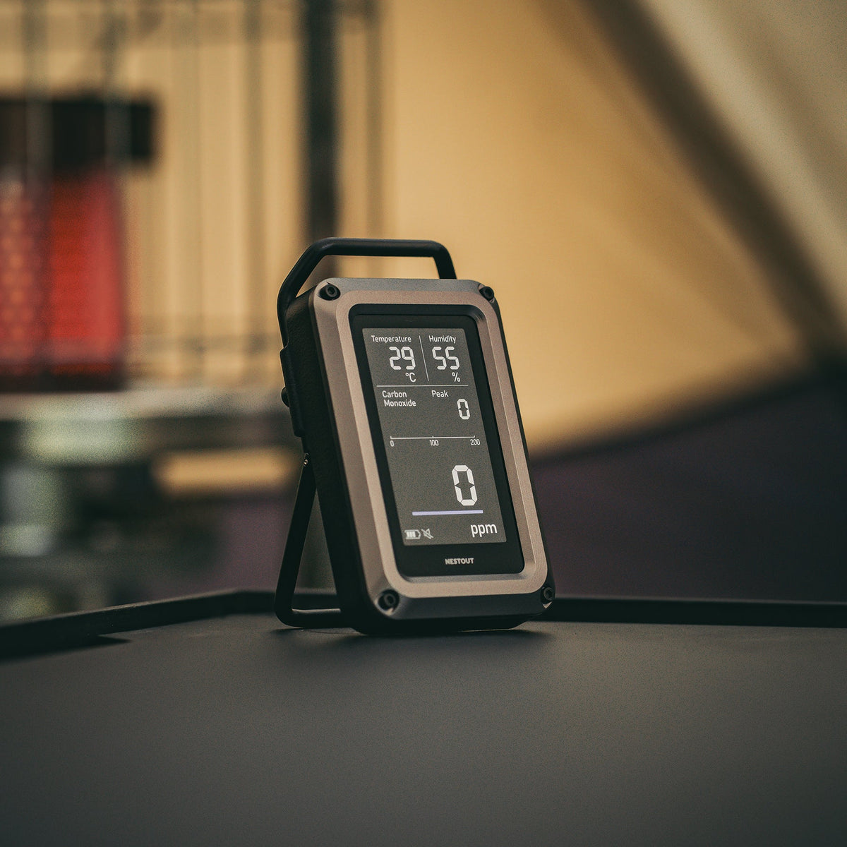 NESTOUT CO Alarm propped on its kickstand outdoors near a tent, screen showing 29°C, 55% humidity, and 0 ppm carbon monoxide