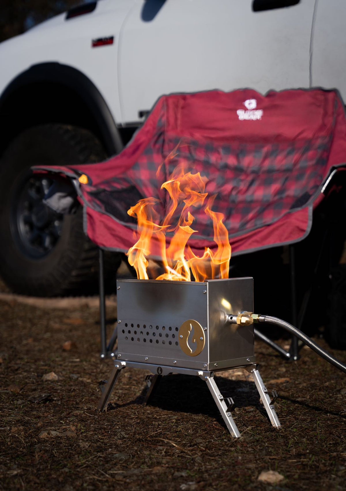Outdoor photo of a firebox burning brightly, set up next to a camp chair with a blanket draped over it