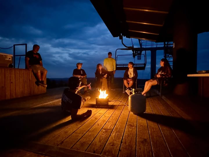 Nighttime lifestyle photo of a group gathered around a lit fire pit on an elevated wood deck overlooking a valley