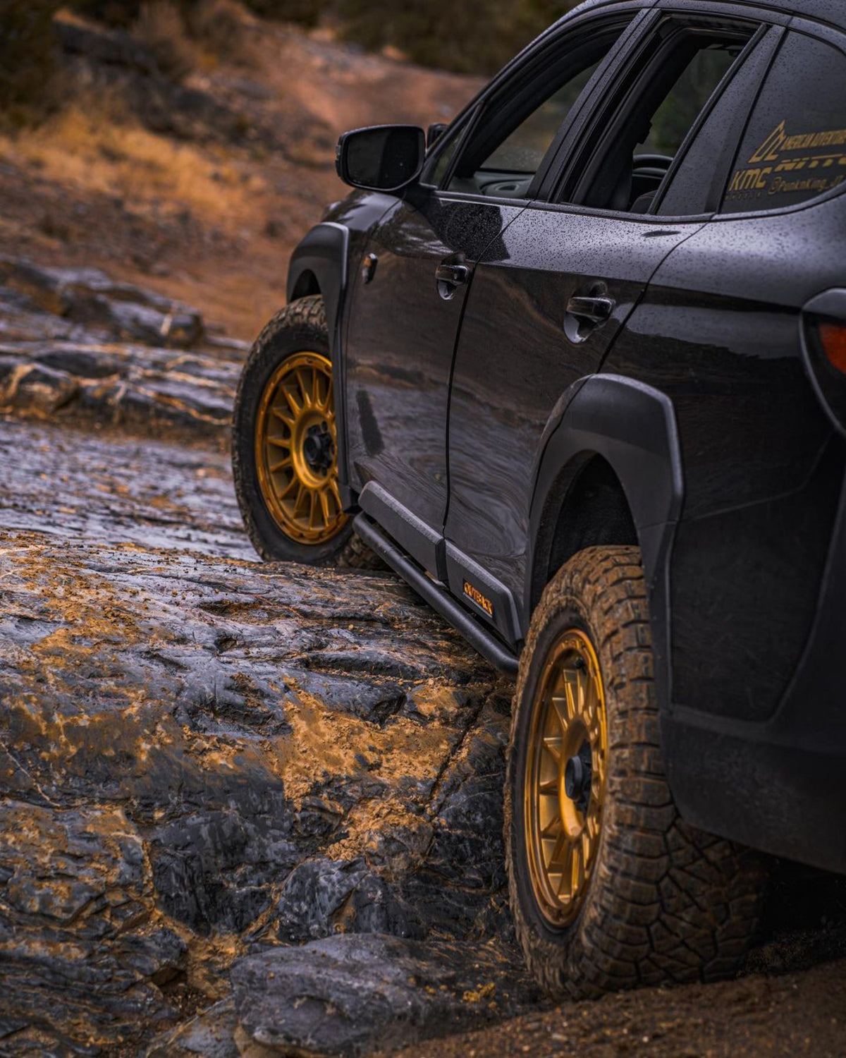 Dark wagon with gold wheels driving through mud on a rocky trail