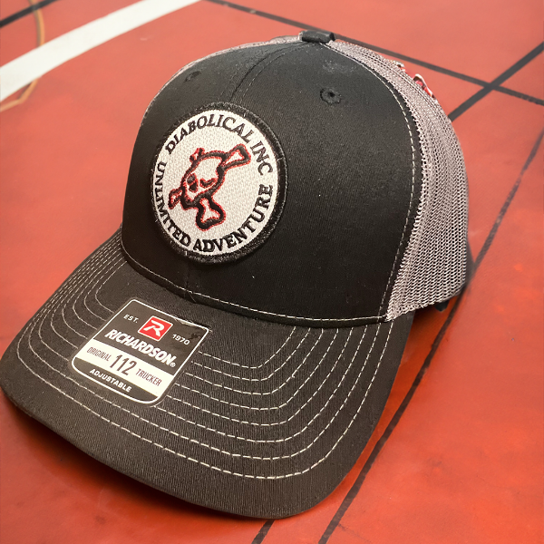 Black-front Diabolical Inc trucker hat with gray mesh on a red surface