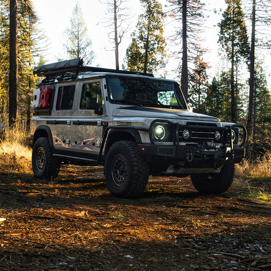Silver SUV with a black bull bar and roof rack parked in a forest