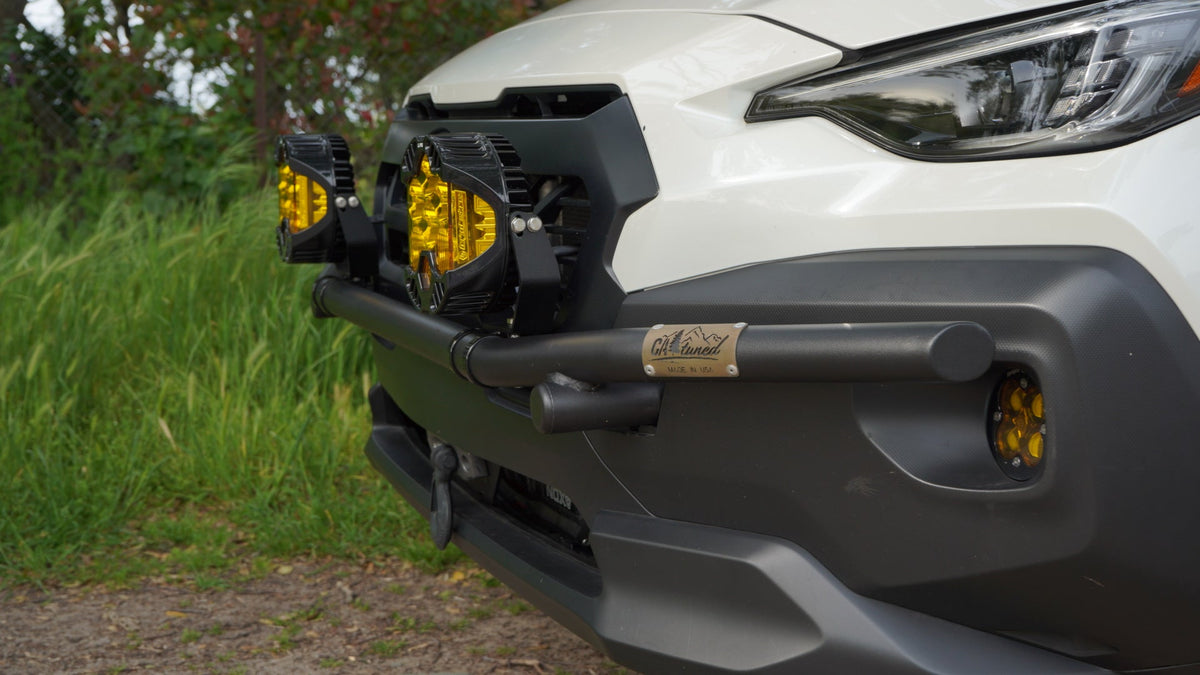 Black brush bar with amber light pods on the front of a white Subaru SUV with grass behind