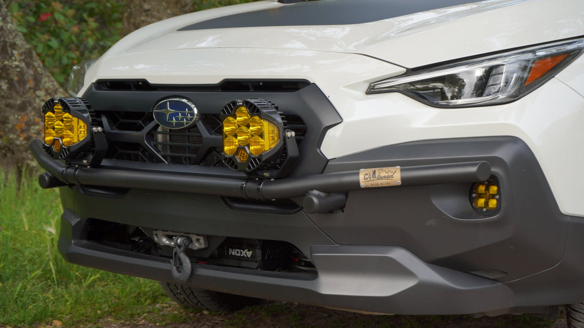 Front of a white Subaru SUV with a black brush bar and amber light pods at the grille