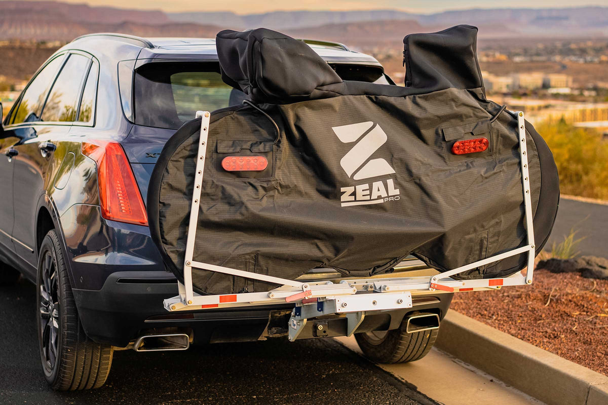 Road bike in a ZEAL Pro cover on a hanging hitch rack behind an SUV at sunset