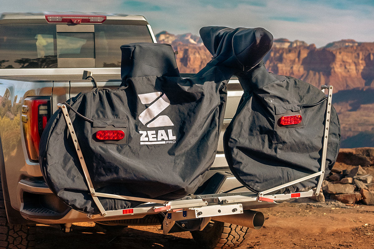 Two mountain bikes in ZEAL Pro covers on a hanging hitch rack behind a pickup in red-rock country