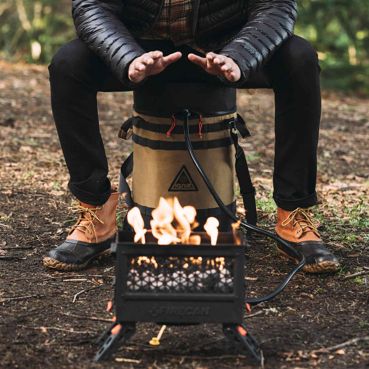 Ignik 20lb tank case seat – person sitting on the case beside a fire pit