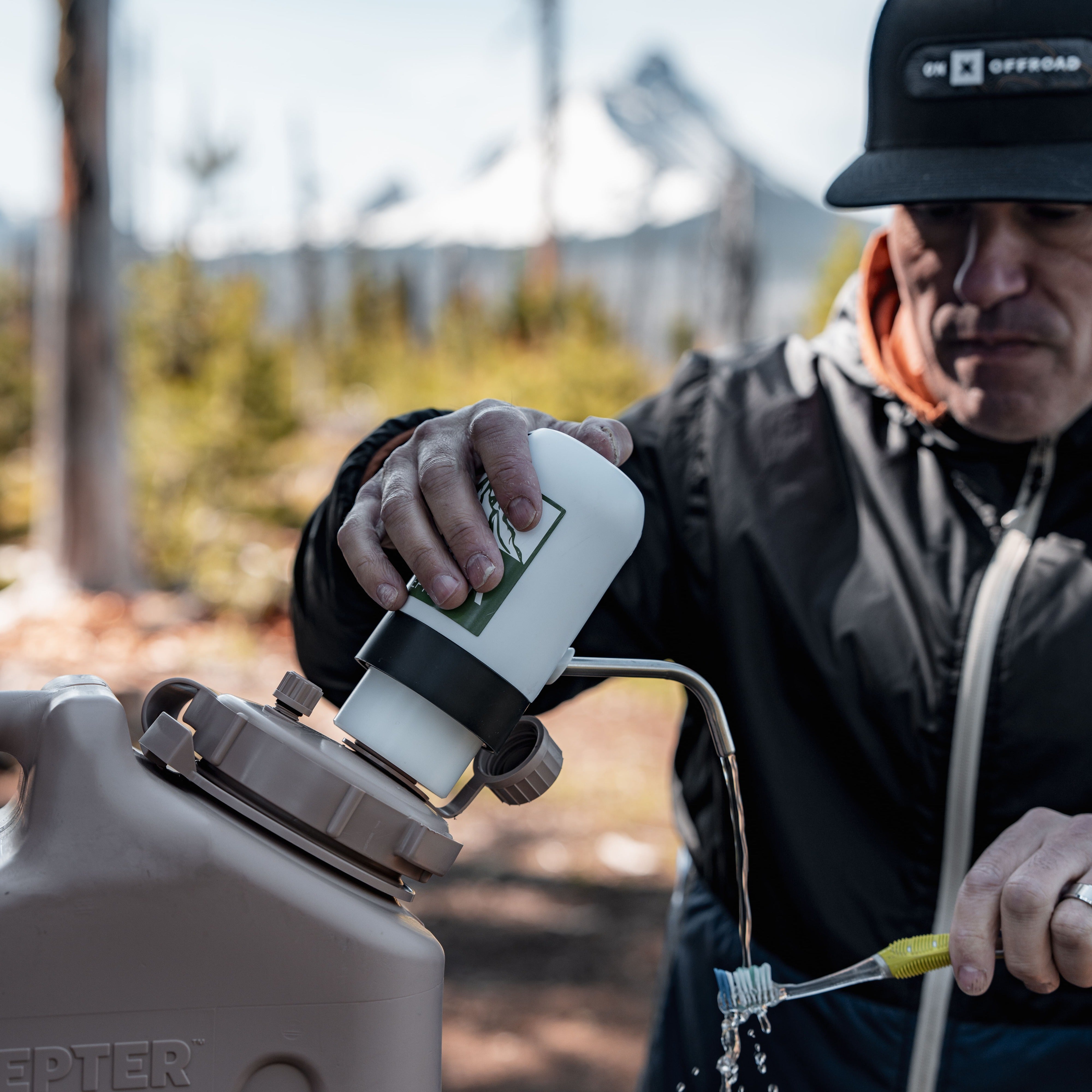 Camper brushing teeth using the Lone Rock Concepts pump on a tan Scepter water can with snowy mountains behind