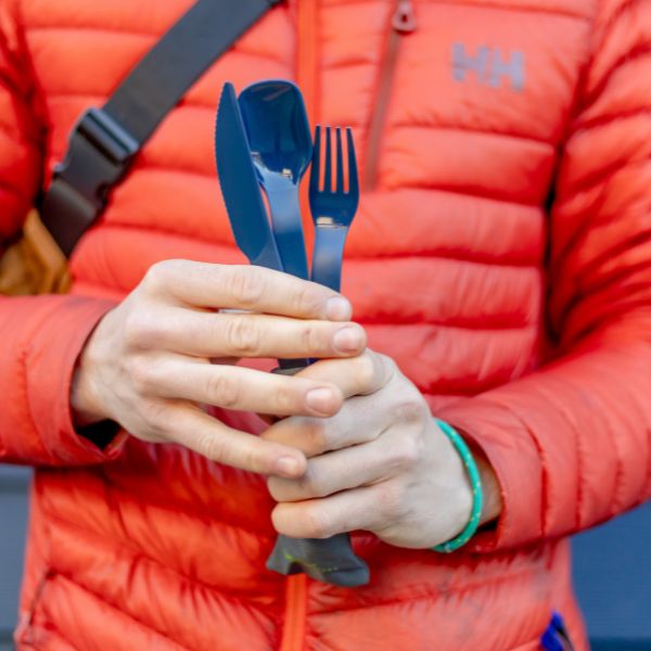 Close-up of a hand holding a fork from the UCO ECO utensil set, wearing an orange jacket