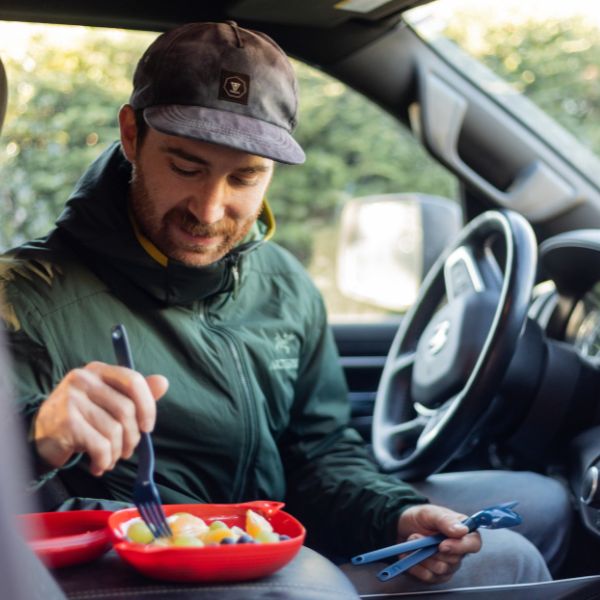 Man eating from a red container while seated in a vehicle