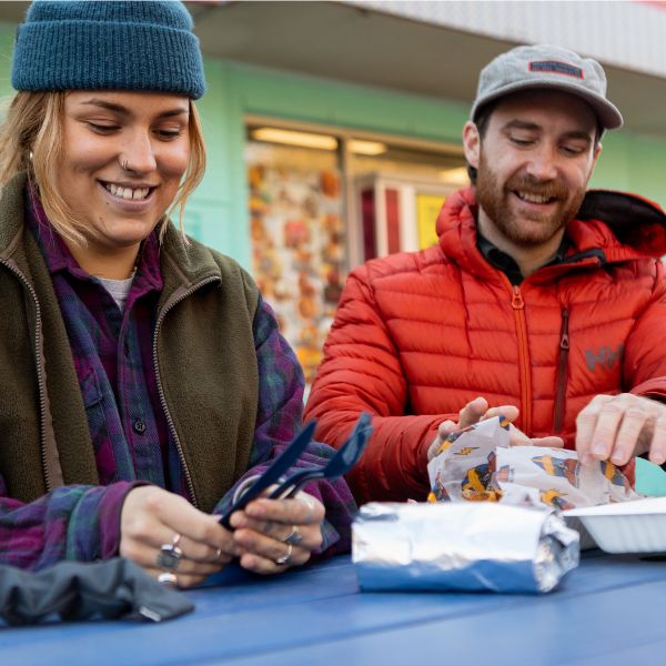 Woman and man smiling while eating outdoors near a shop