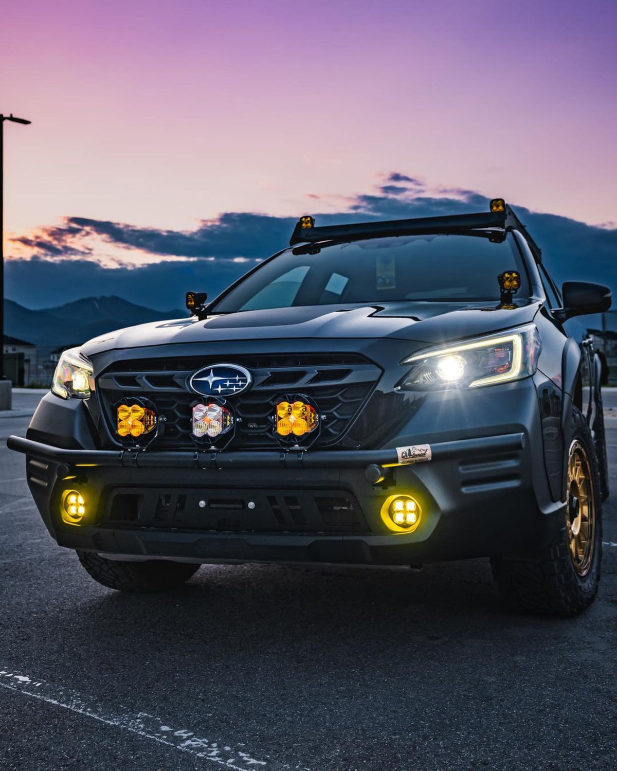 Dark Subaru wagon at dusk with amber and white light pods at the front