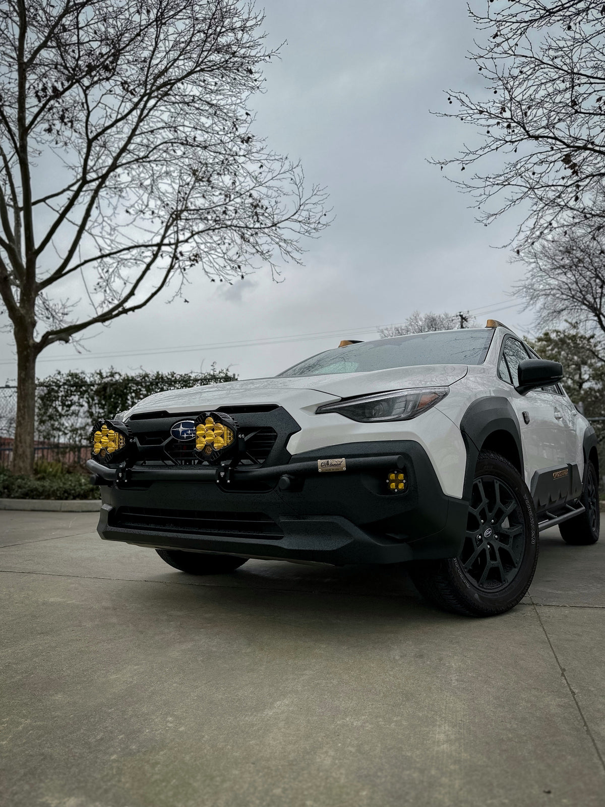Front three-quarter view of a white Subaru SUV with a black brush bar and amber lights