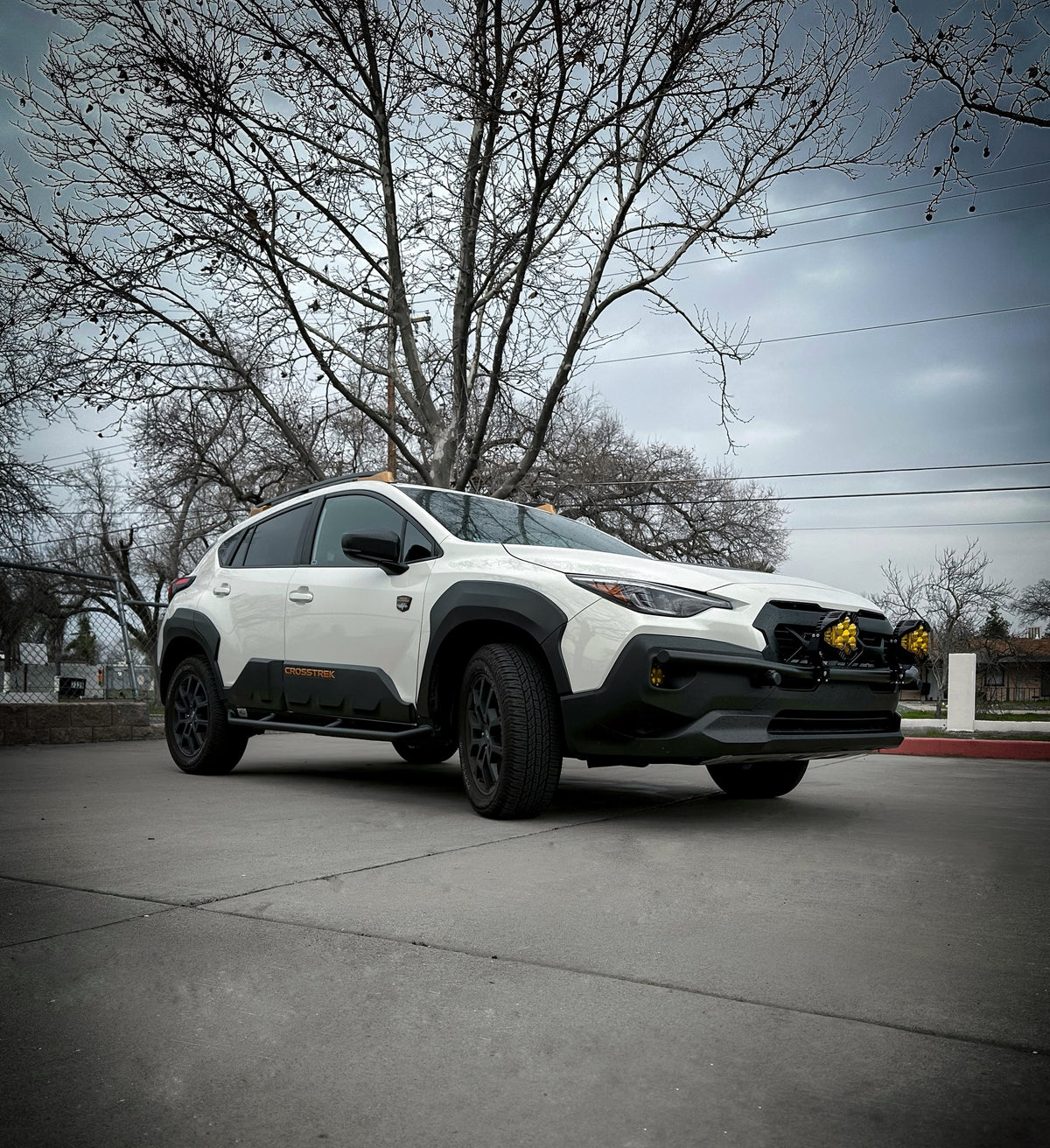 White Subaru SUV parked on a street with black rock sliders