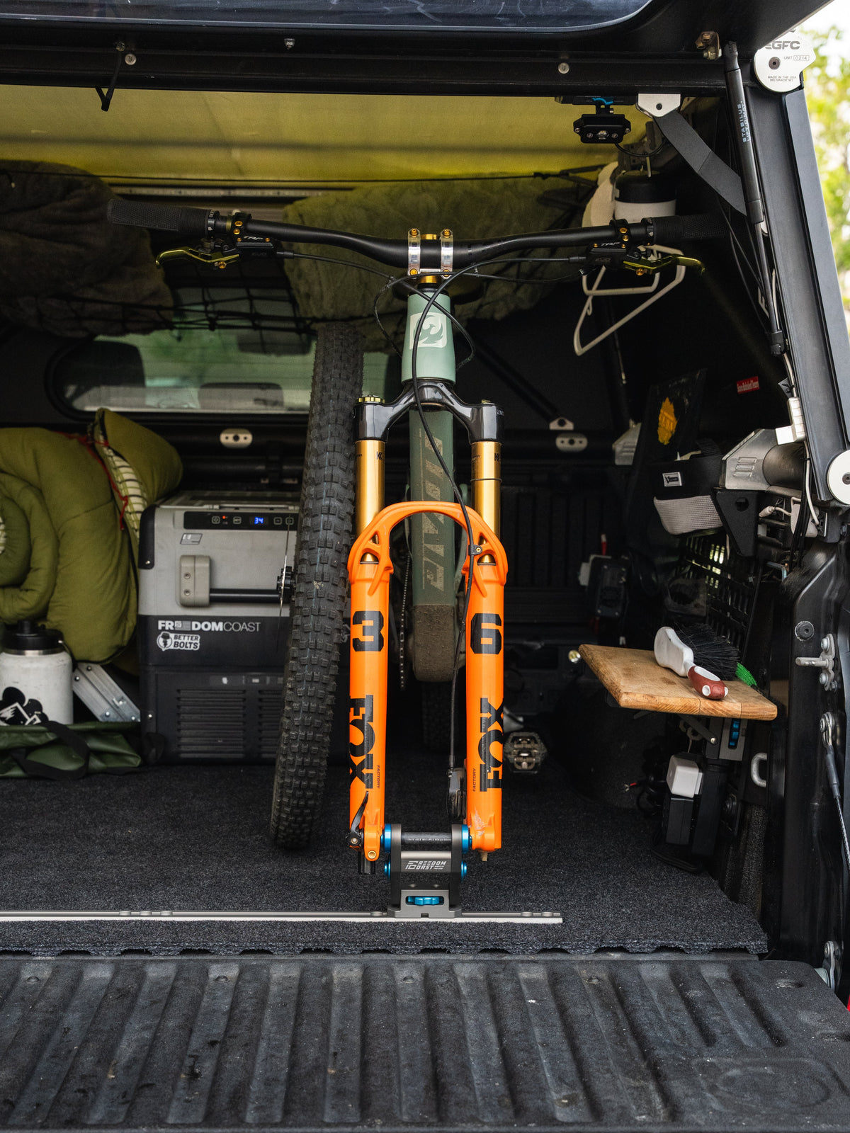 Freedom Track installed across a Toyota truck bed holding an orange mountain bike by the fork
