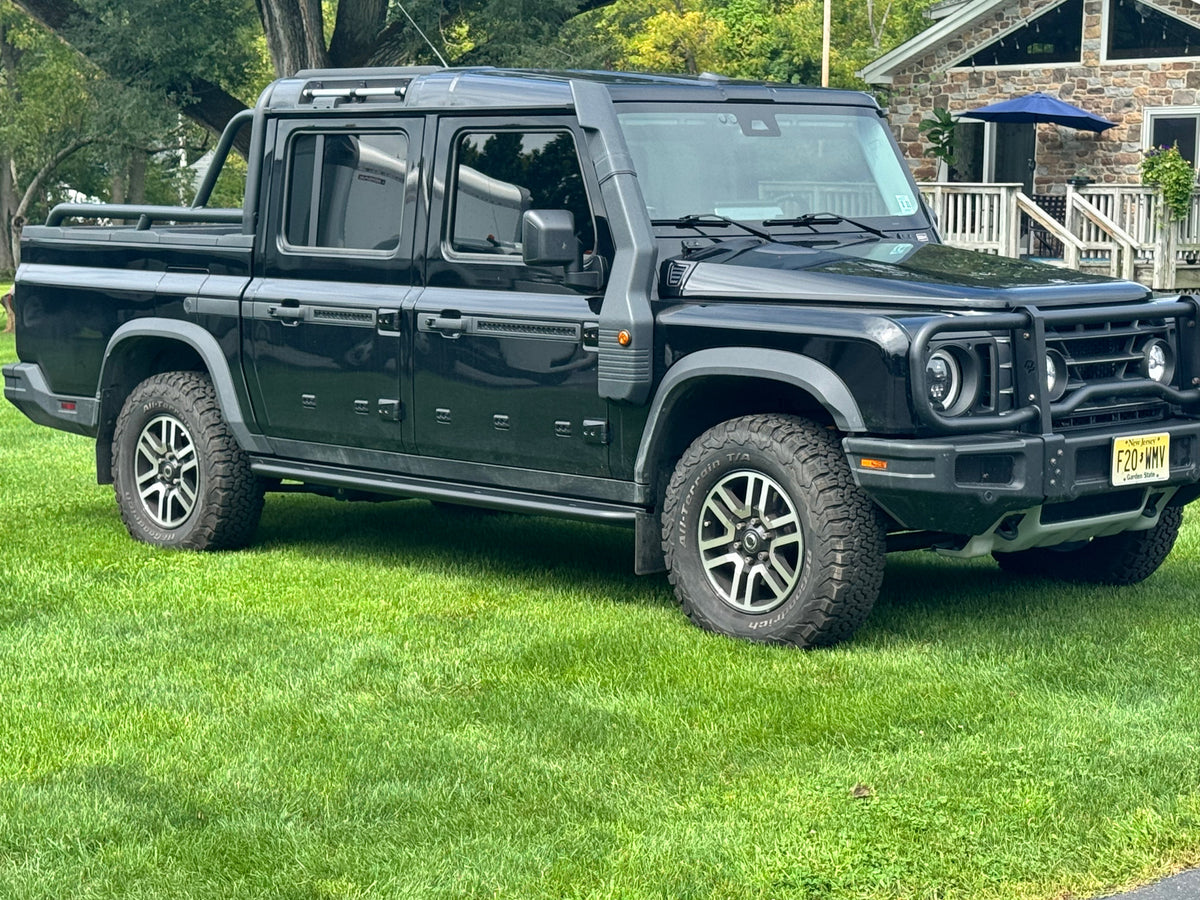 Black INEOS Quartermaster pickup parked on grass with rock sliders fitted