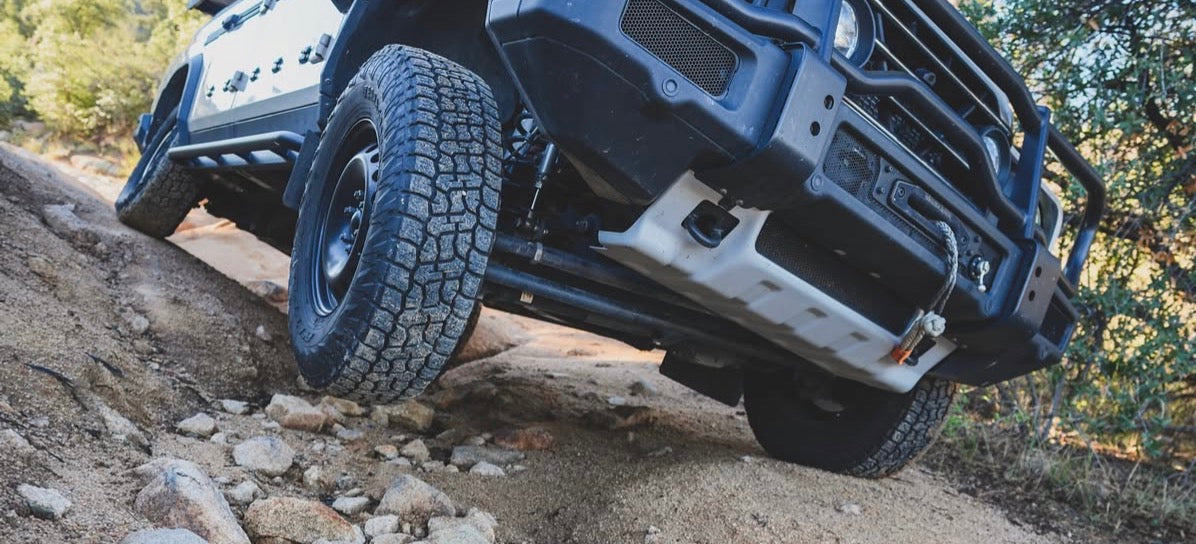Front end of an INEOS vehicle climbing over rocks, shot from a low angle