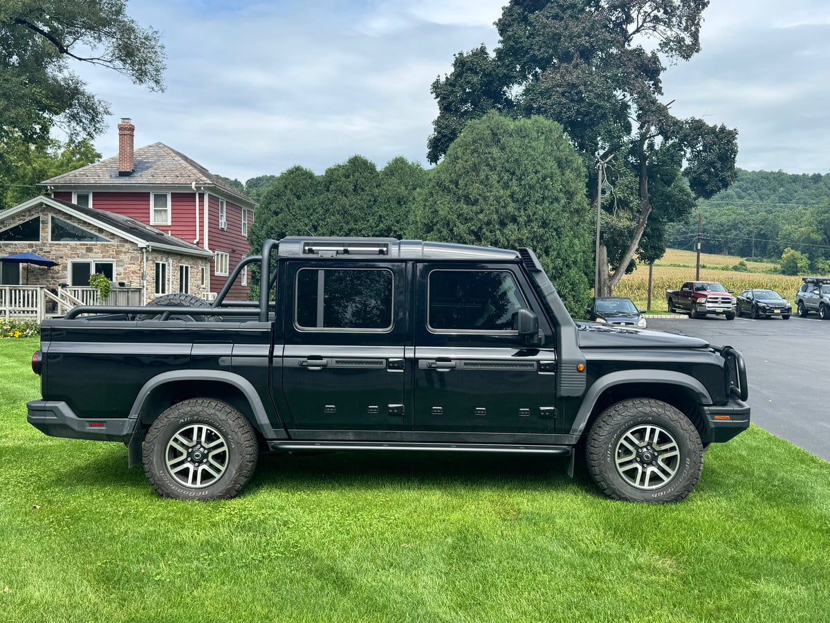 Side profile of a black INEOS Quartermaster pickup with rock sliders on grass