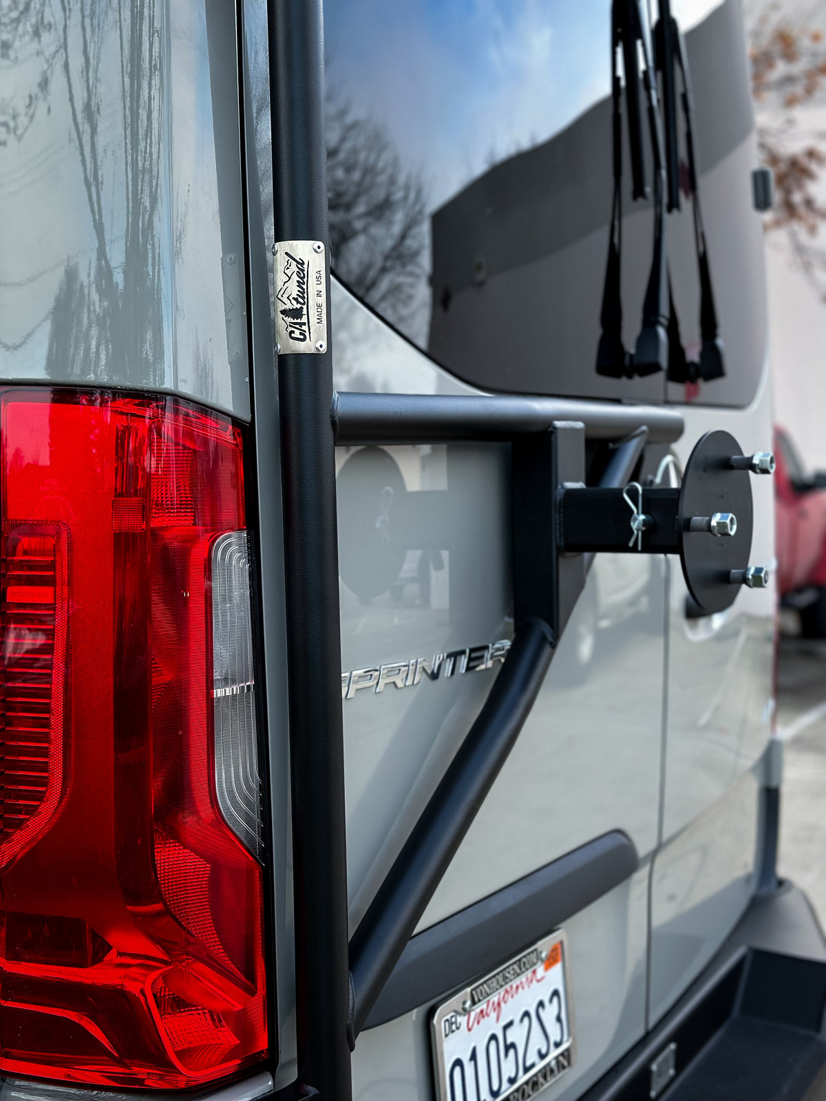 Tire carrier arm and rear door of a gray van beside a tail light