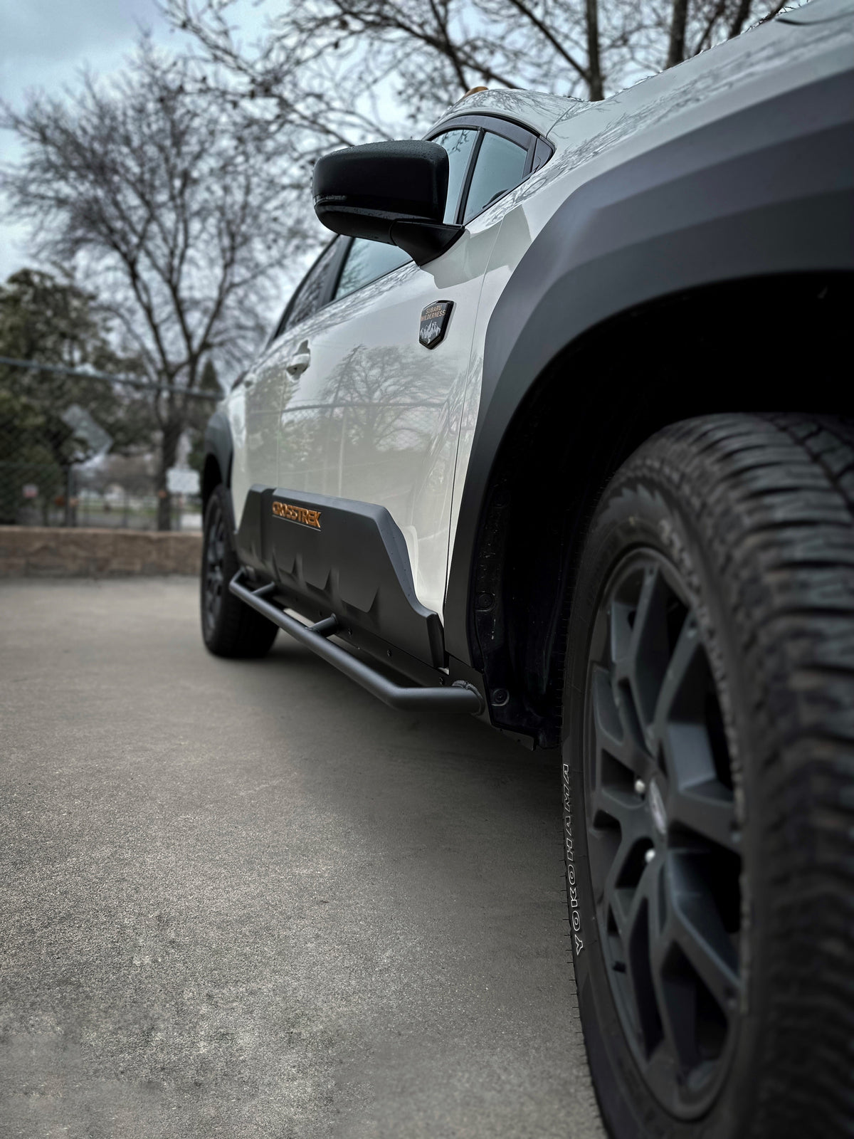Front wheel area of a white SUV with a black rock slider tube along the rocker