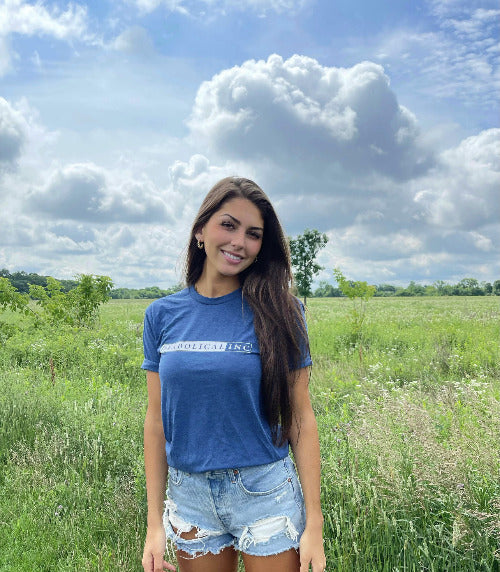 Woman in a field wearing the heathered blue Diabolical Inc T-shirt
