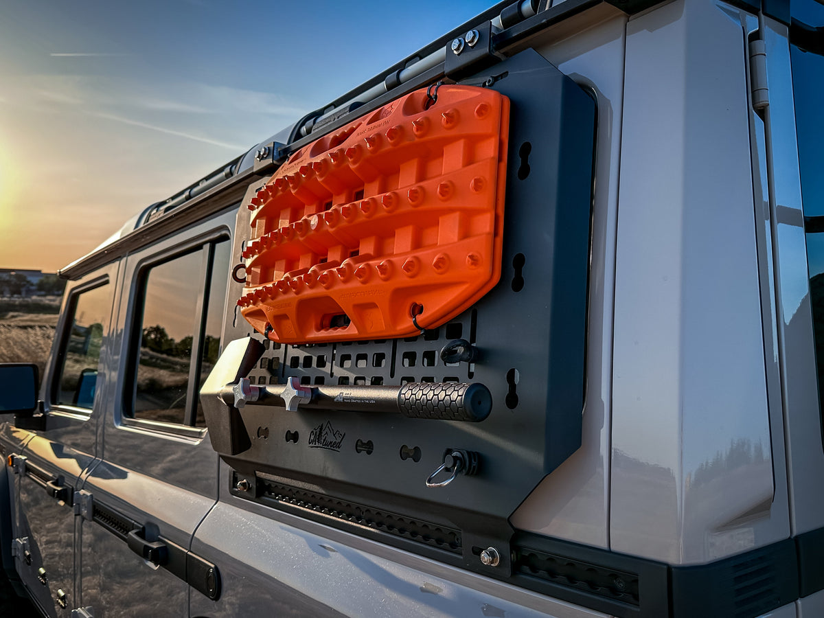 Orange recovery boards and gear mounted on the MOLLE panel, lit by sunset