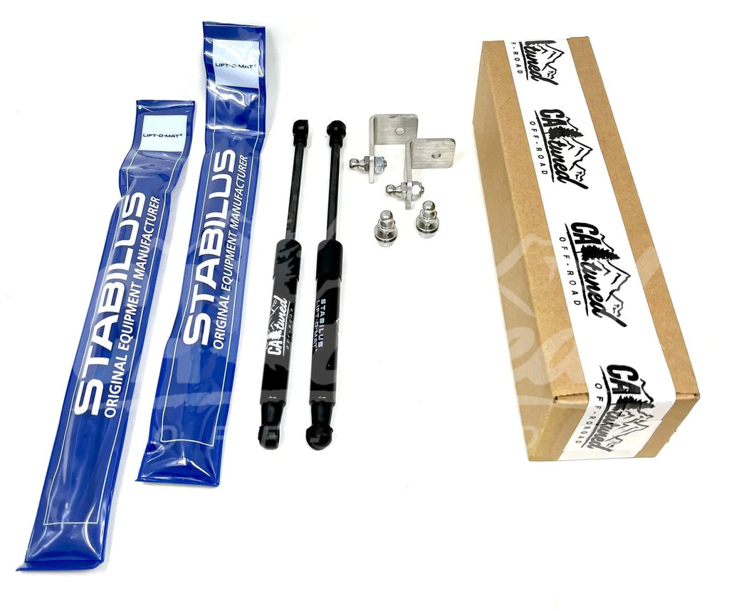 Pair of gas hood struts with mounting brackets and hardware beside their packaging and box