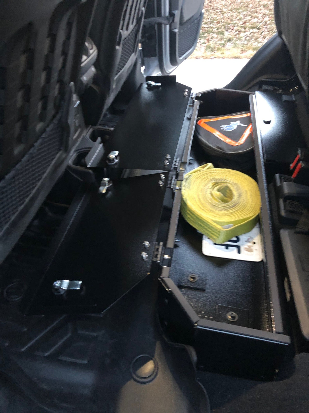Gladiator lock box under the lifted rear seat with one lid open showing a recovery strap