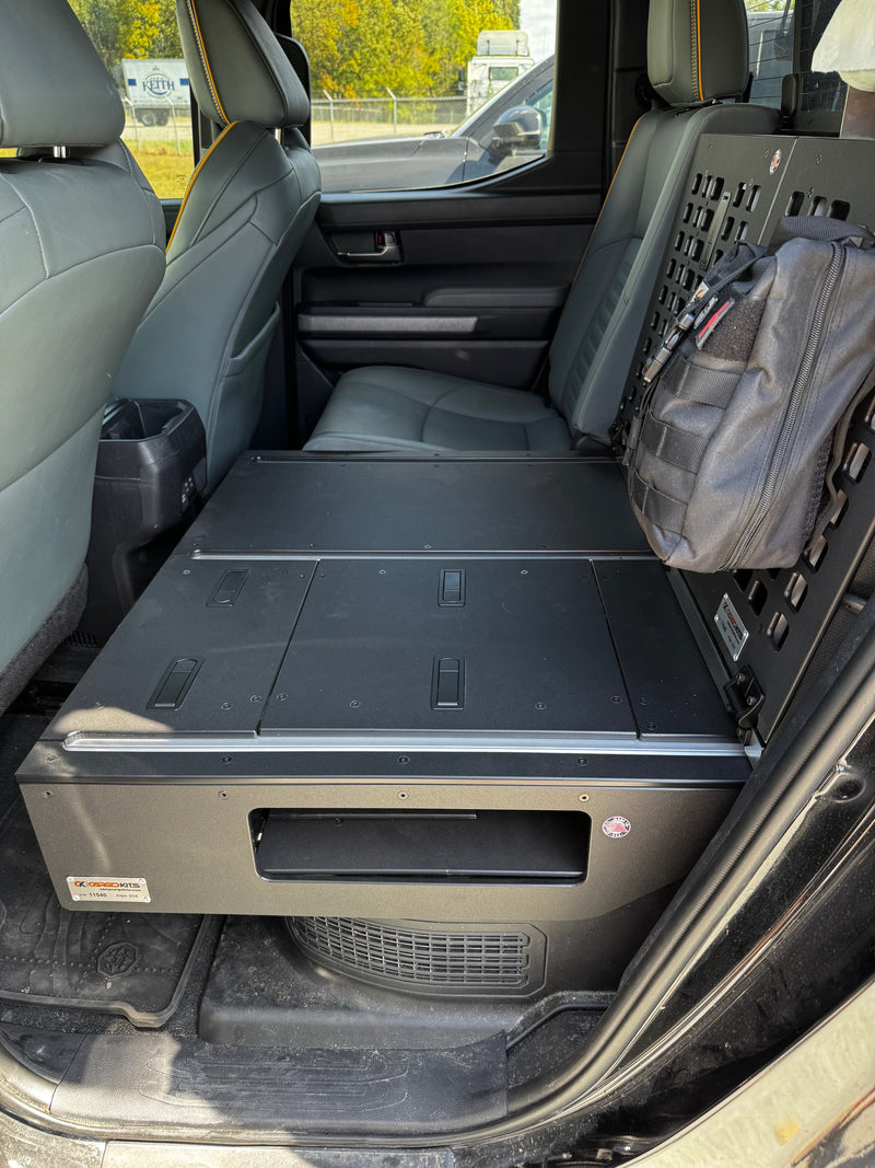 CargoKits aluminum seat delete platform installed in the rear seat area of a crew cab truck, with a drawer-style storage front, top access hatches, and a MOLLE panel holding a first-aid pouch
