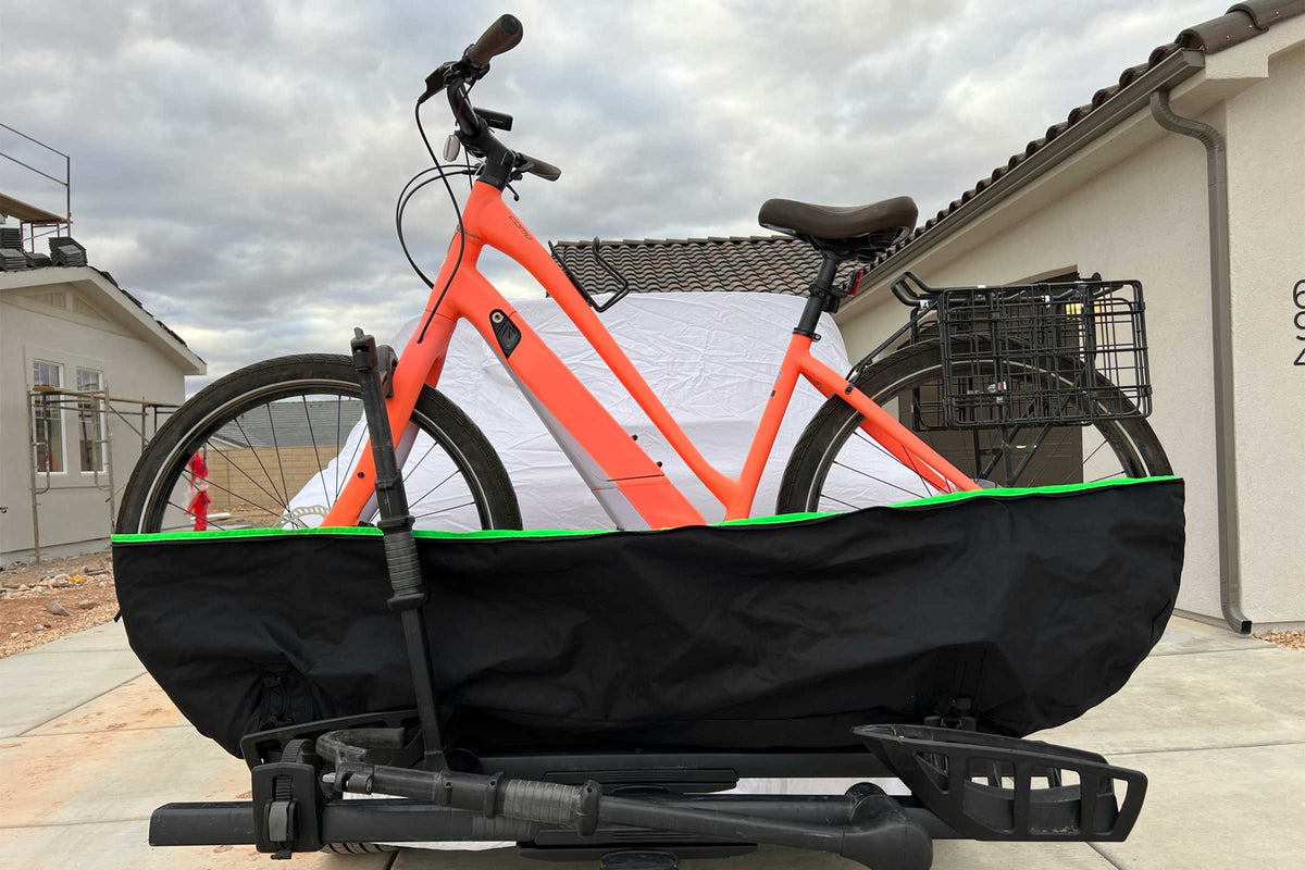 Orange step-through e-bike resting in the lower section of the two-piece cover on a tray rack