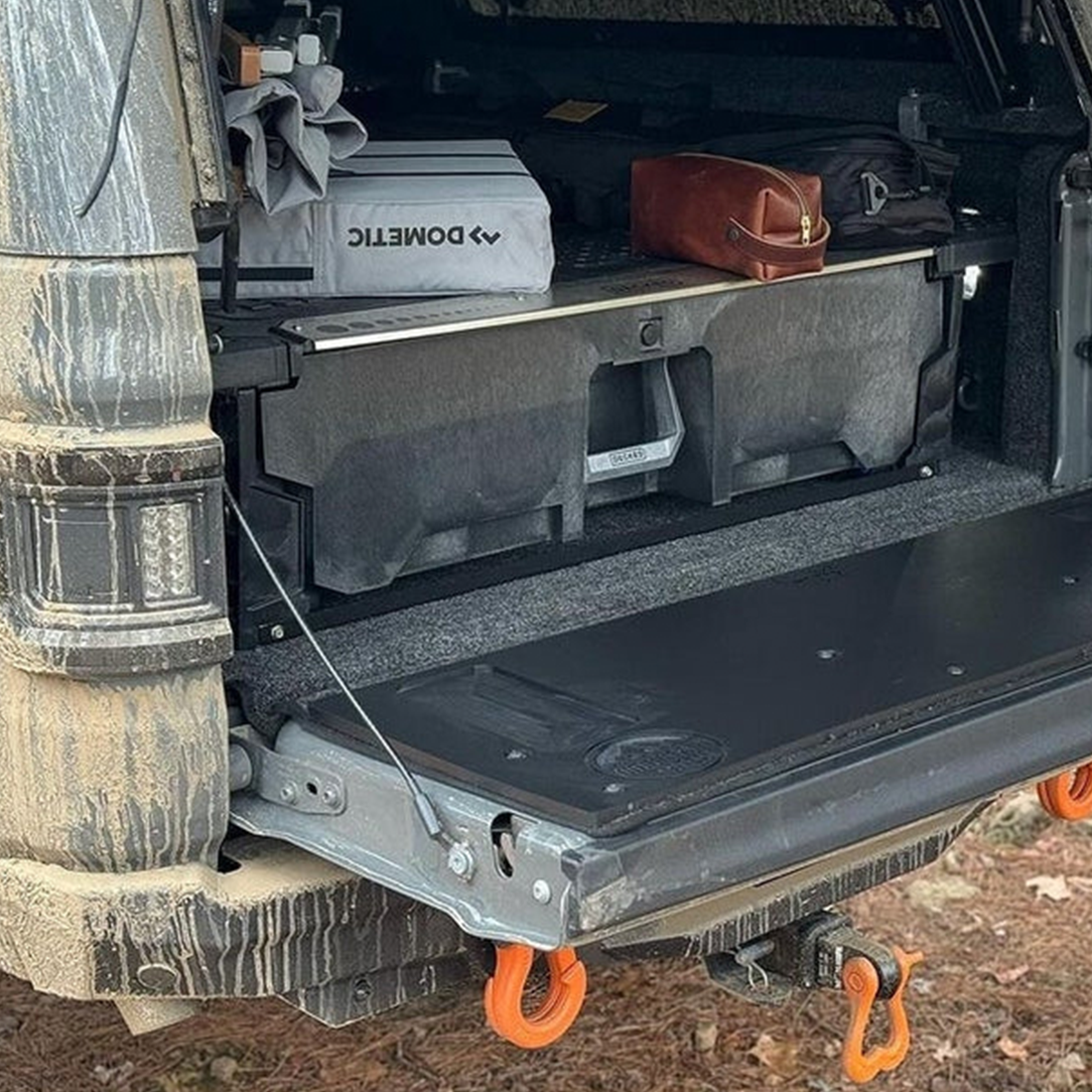 Mountain Hatch tailgate table on a muddy Jeep Gladiator JT tailgate with a bed drawer system and gear behind it