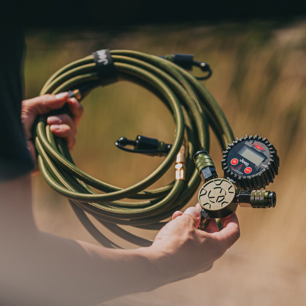 Lifestyle photo of hands holding the coiled hose and Jeep-branded manifold of the Rapid Multi-Tire Air System outdoors
