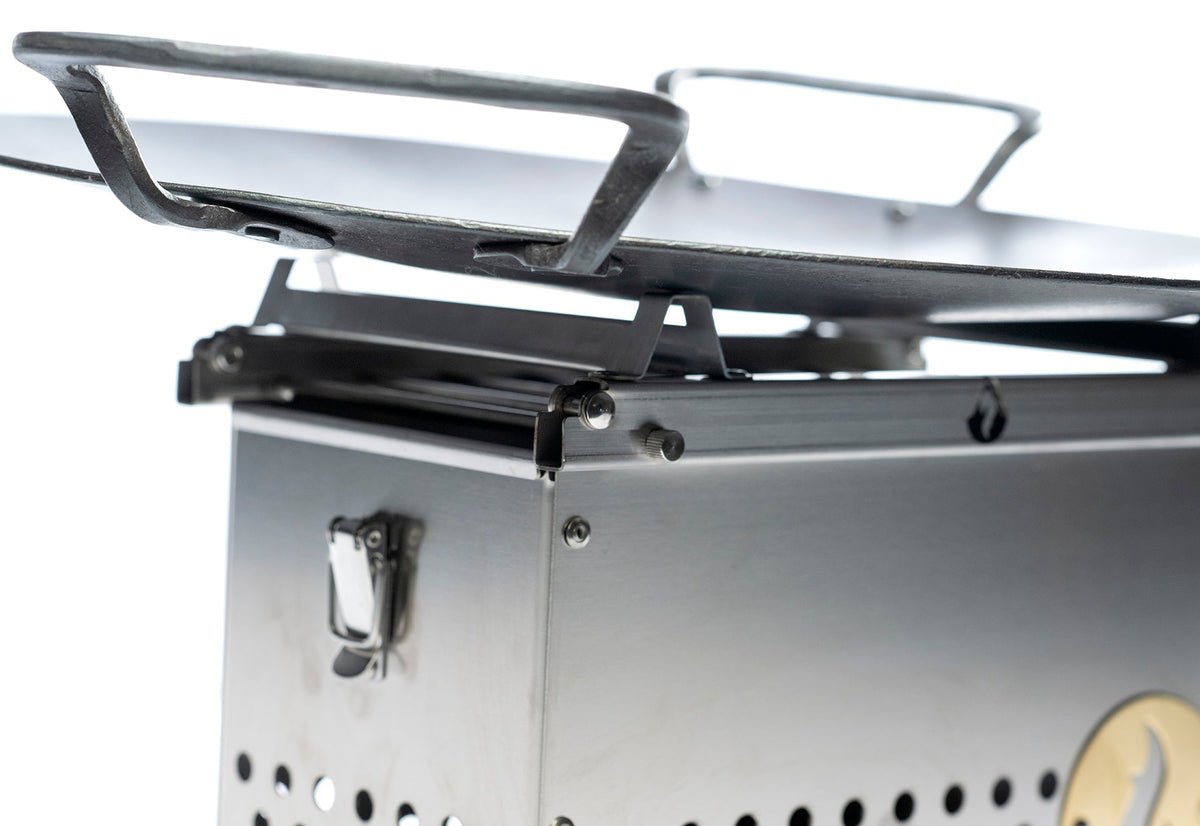 Close-up of the stainless steel firebox's folding leg and stand hinge mechanism with top grate, studio shot