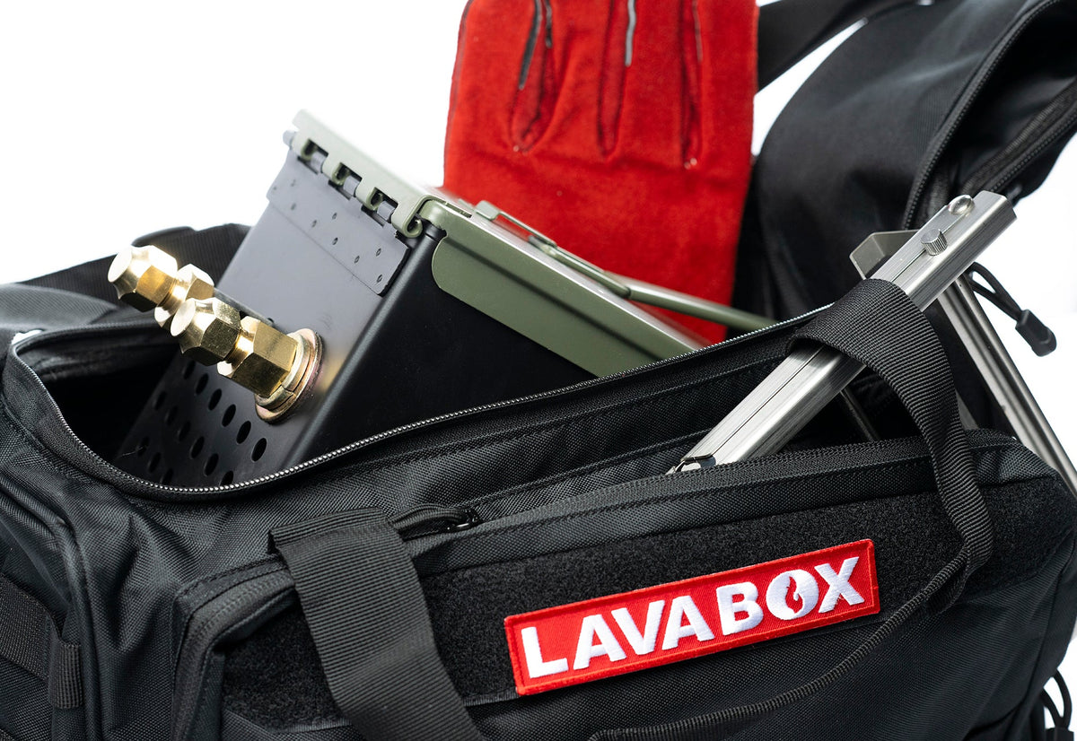 Open black LAVABOX carrying bag packed with a folded stove stand, red fireproof gloves, and a propane regulator hose