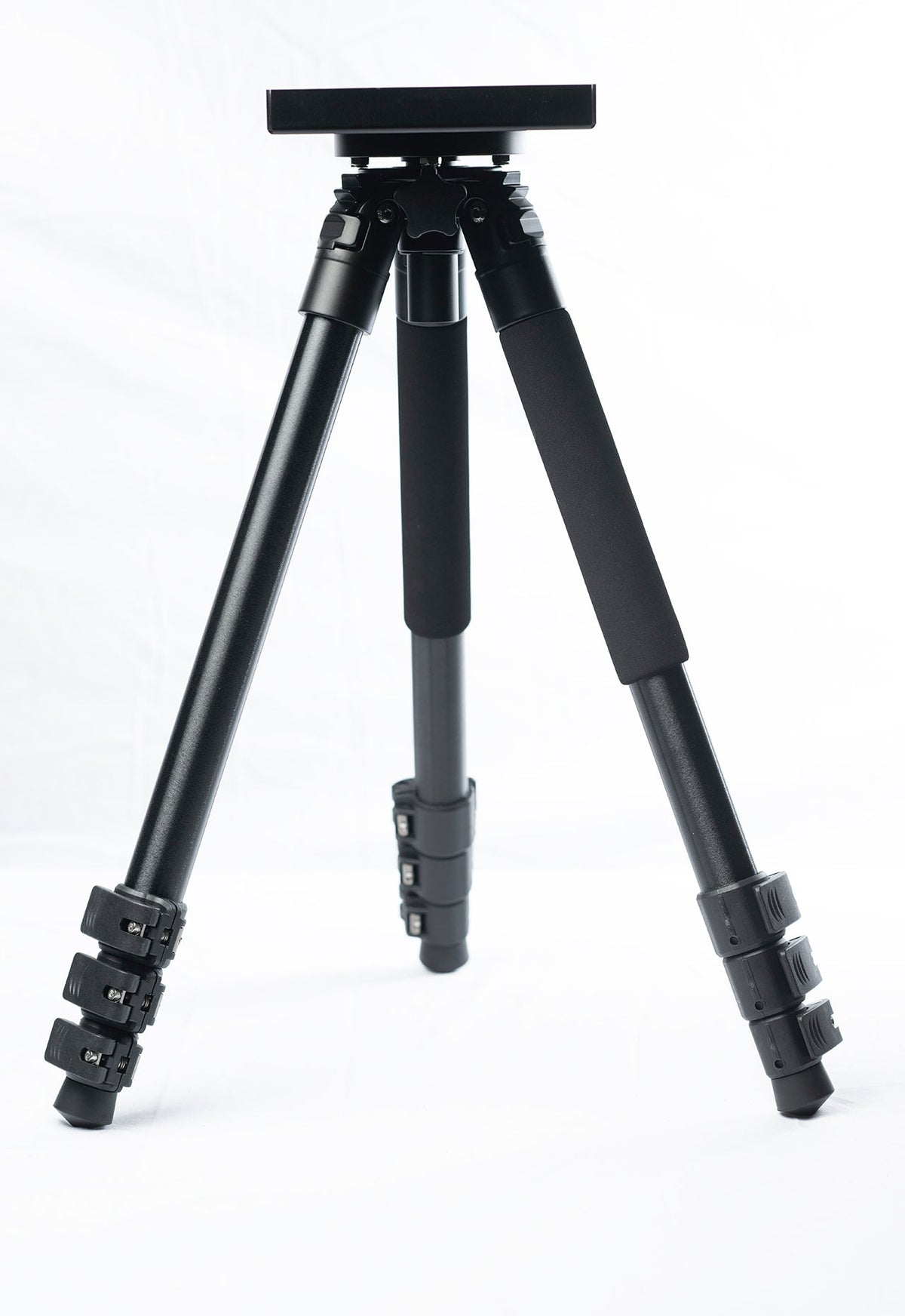 Black tripod stand with a flat mounting plate, legs shown extended, studio shot on white background