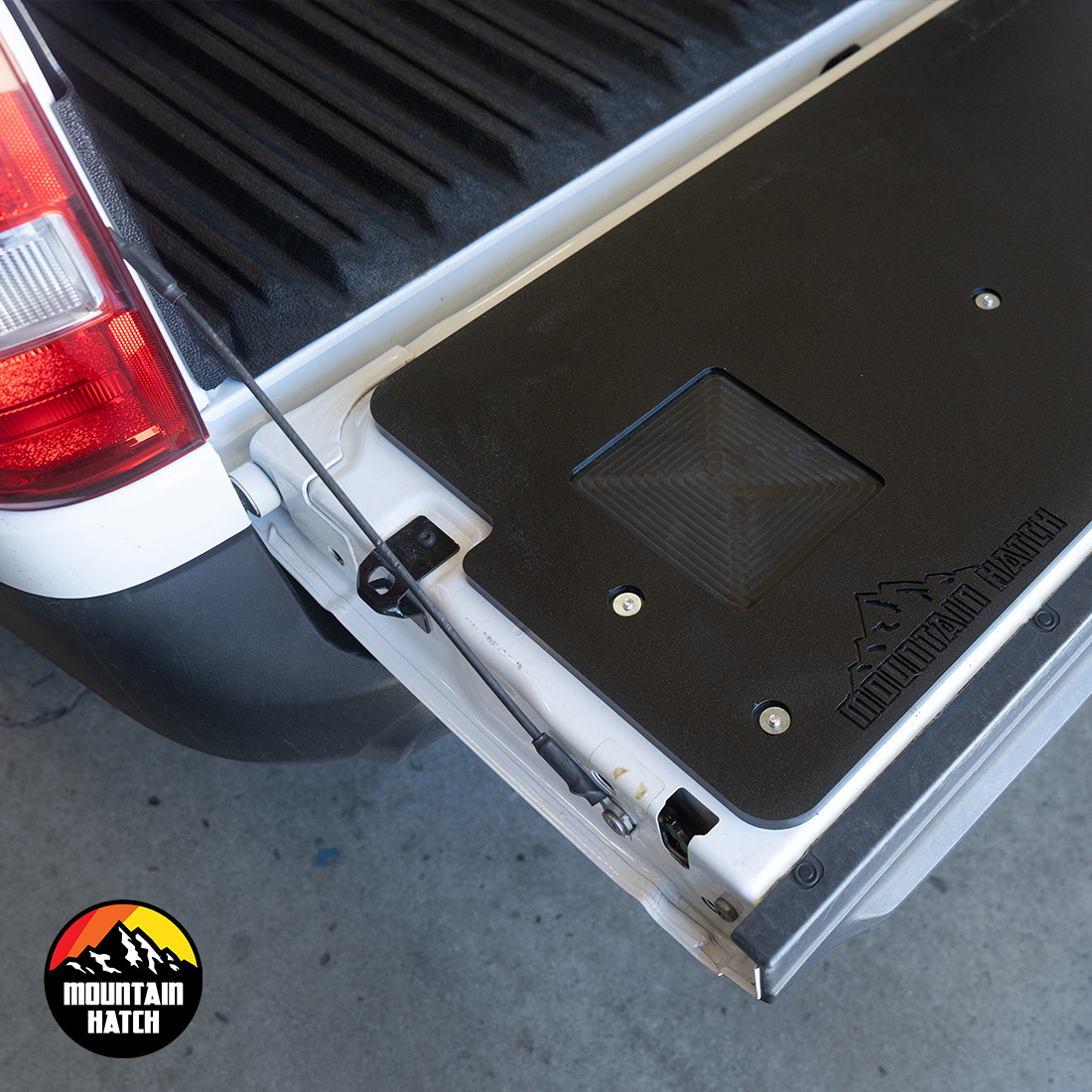 Close-up of the Mountain Hatch tailgate table on a white Ford Maverick tailgate showing the recessed utility tray and stamped logo