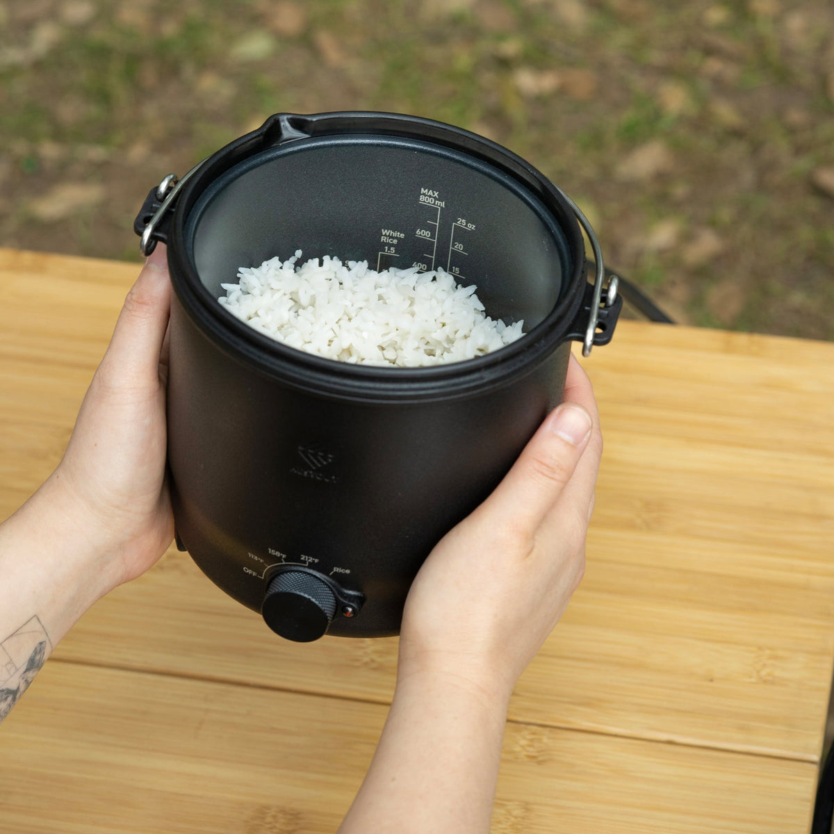 Overhead view of the black NESTOUT cooker's pot filled with cooked white rice, showing the fill-line markings on the lid and the temperature control dial