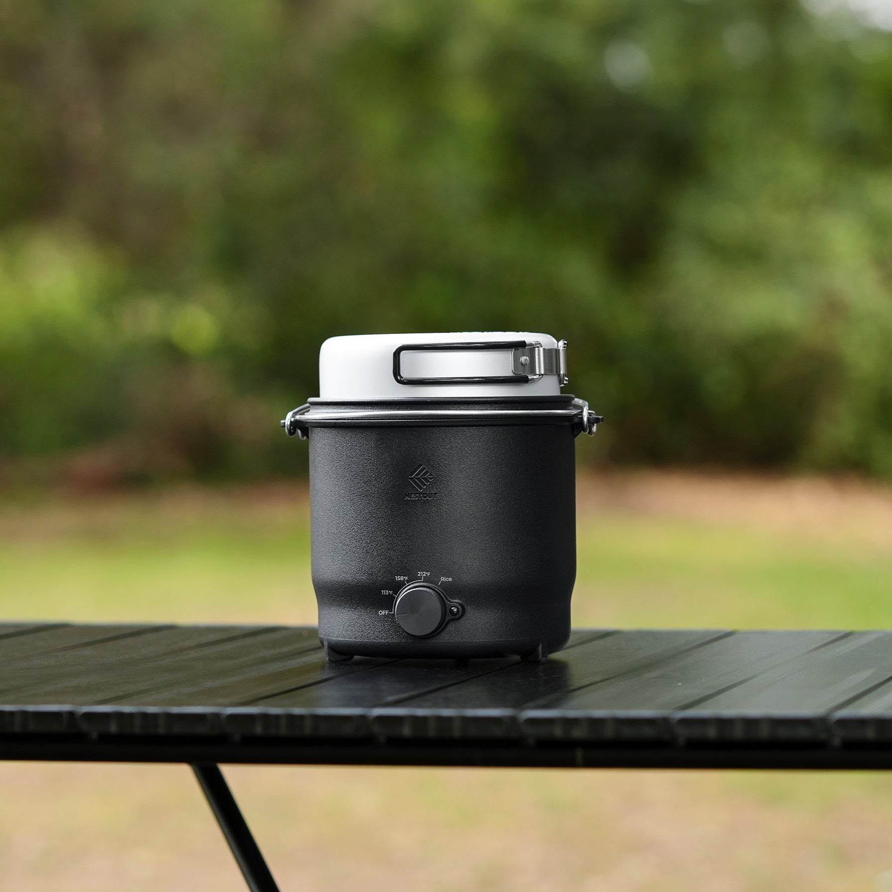 NESTOUT cooker in black with white lid latched, side profile studio shot on an outdoor picnic table