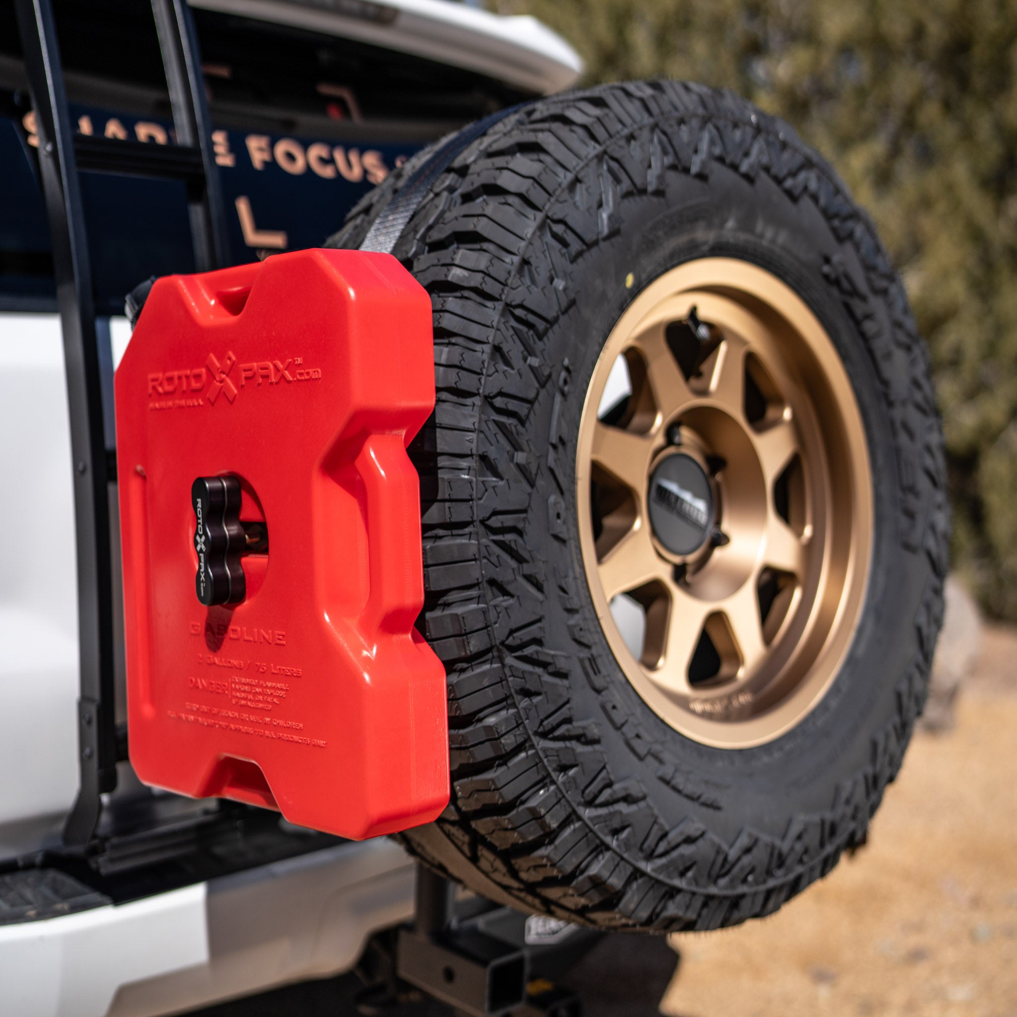 A red Rotopax spare tire mount attached to a vehicle's spare tire, designed to hold a fuel can.