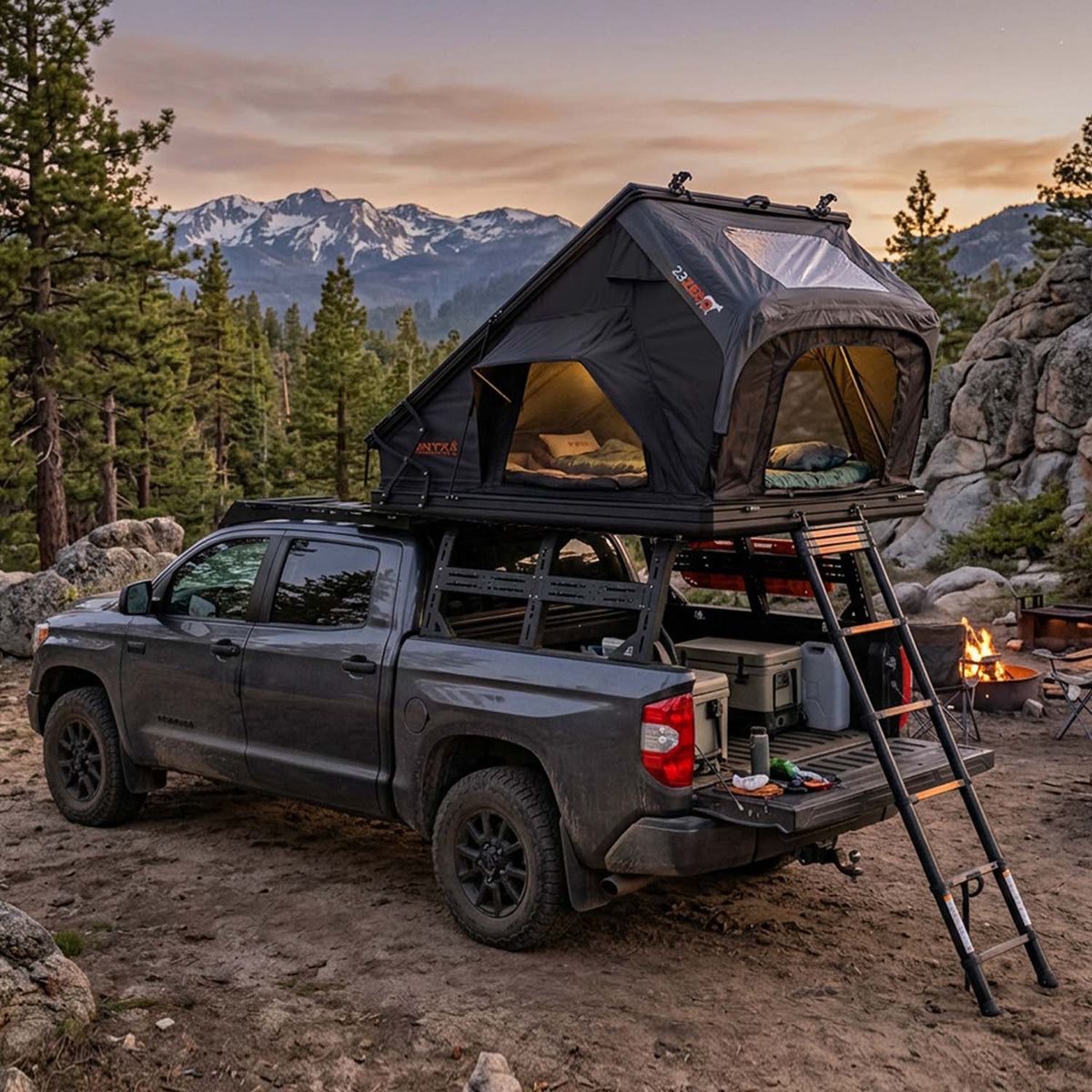 23ZERO Onyx Triple X roof top tent deployed on a Toyota Tundra at dusk in the mountains, with the ladder down and a campfire lit nearby