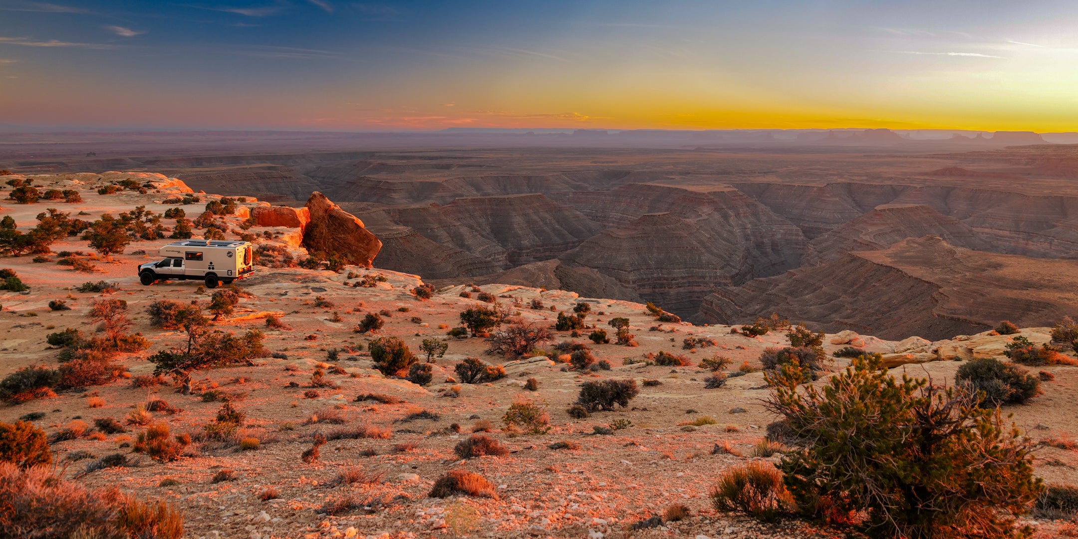 Scenic view of a desert landscape with a EarthRoamer overland vehicle on a cliff at sunset.