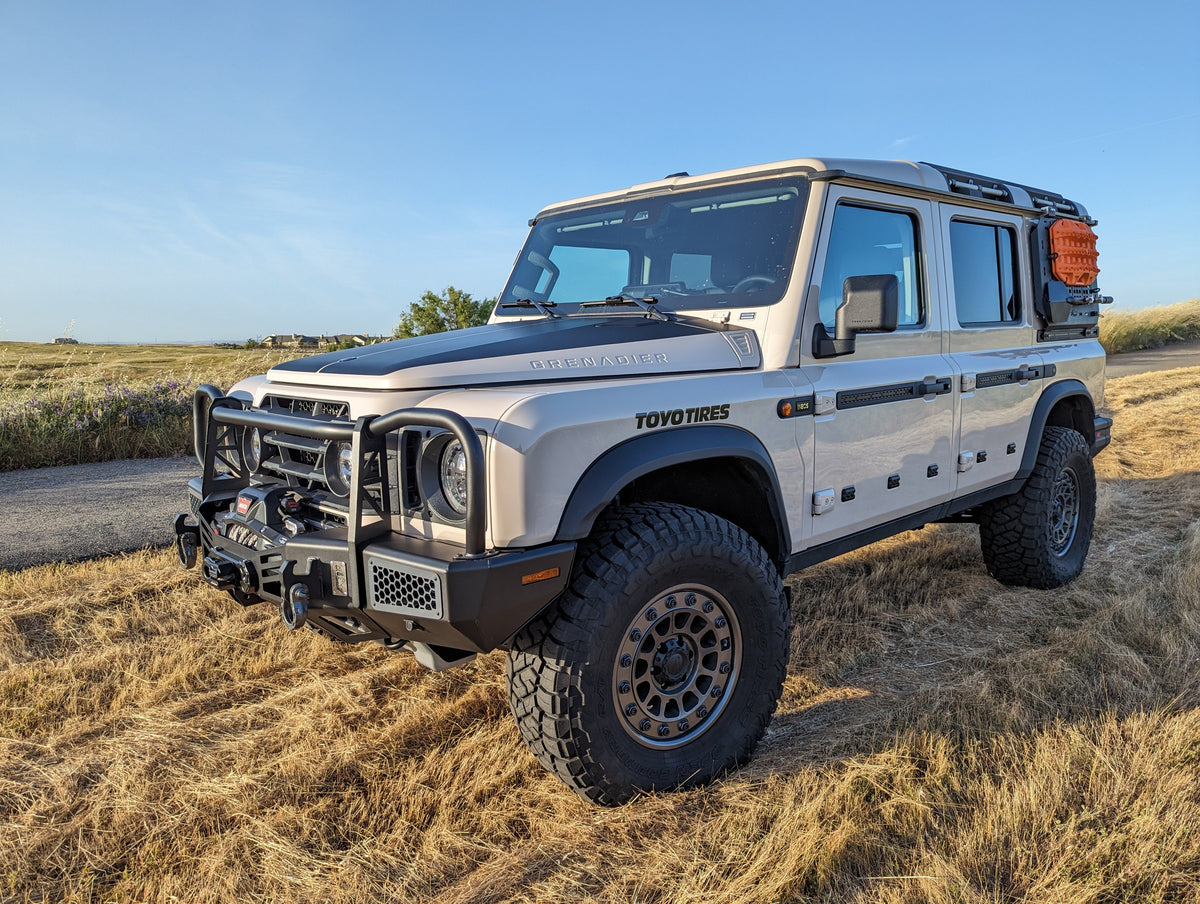 Silver SUV with a bull bar and roof rack parked in a grassy field