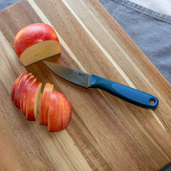Hand slicing an apple with the UCO Camp Paring Knife on a blue plate outdoors