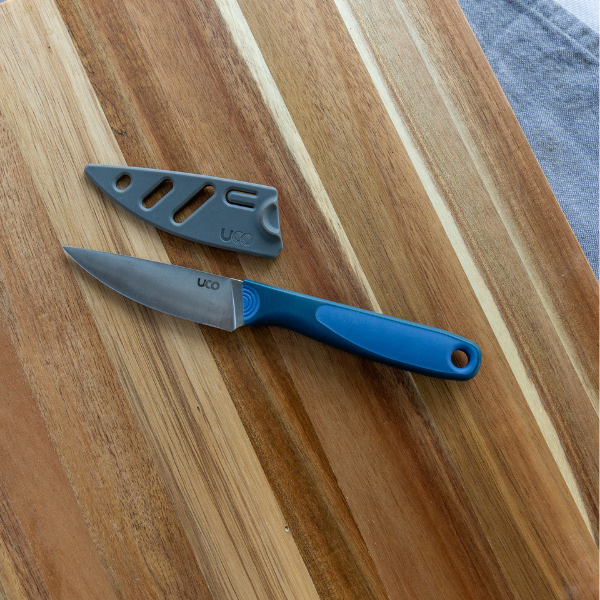UCO Camp Paring Knife and its sheath resting together on a wood cutting board