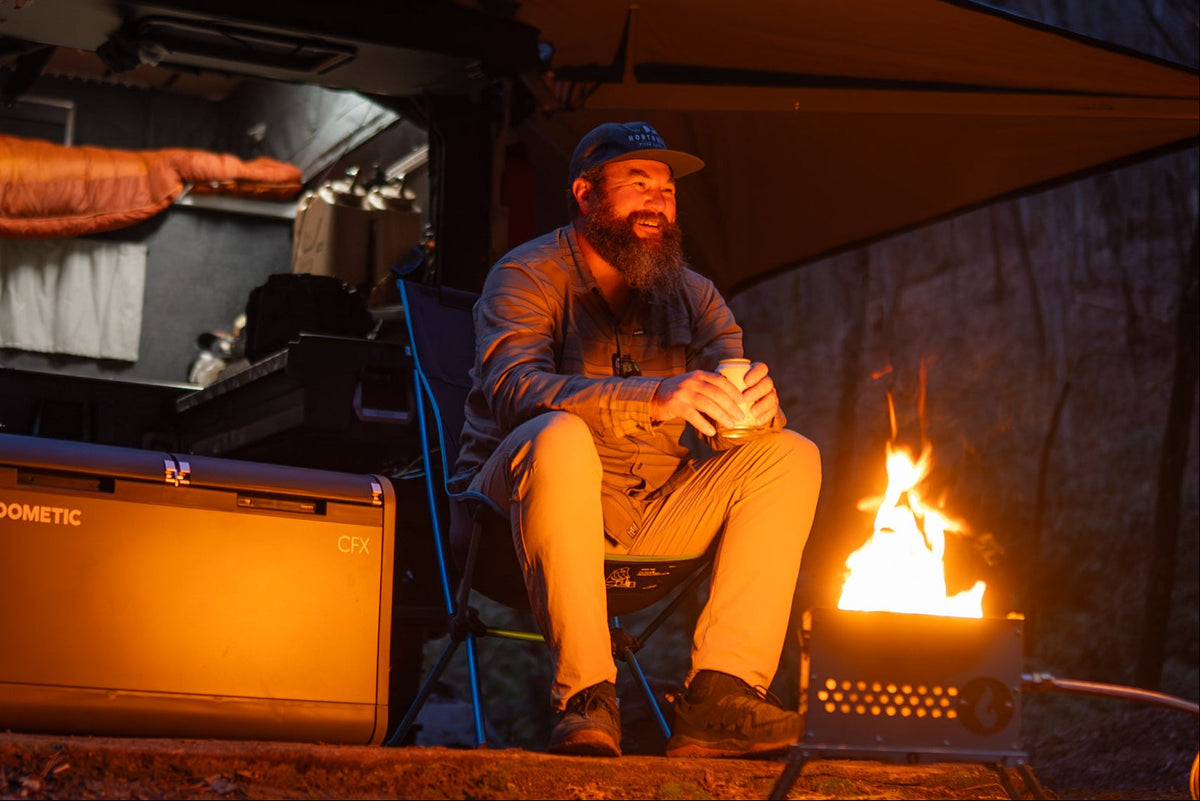 Nighttime lifestyle photo of a person warming their hands by a lit LavaBox firebox next to a camp trailer